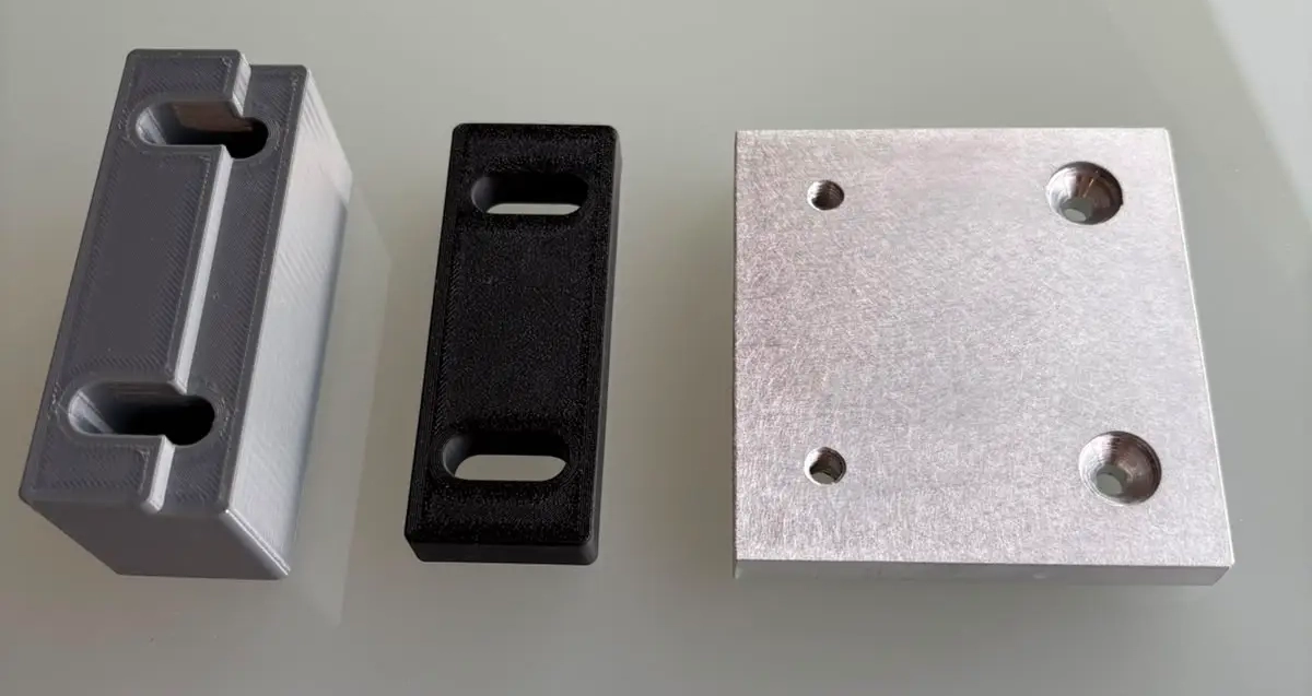 Verschiedene Varianten 3D-gedruckter Abstandshalter und Montagehilfen neben einer Aluminium-Referenzplatte in der Lohnfertigung der S2S Systemdrucker GmbH