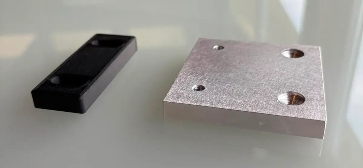 Im 3D-Druck gefertigtes Kunststoffbauteil neben einer Aluminium-Referenzplatte aus der Lohnfertigung der S2S Systemdrucker GmbH